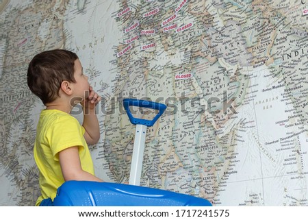 A boy in a yellow t-shirt with a blue suitcase is looking at a world's map. Selective phocus. The concept of closed borders of Europe, the cancellation of vacation.