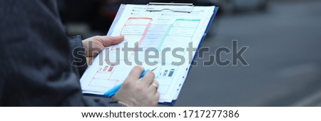 Close-up of male hands holding clipboard with documentations and writing down something. Accident statement document used after car crash. Road risk and incident concept Royalty-Free Stock Photo #1717277386