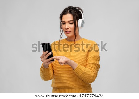 people, technology and audio equipment concept - young woman with pierced nose in headphones listening to music on smartphone over grey background