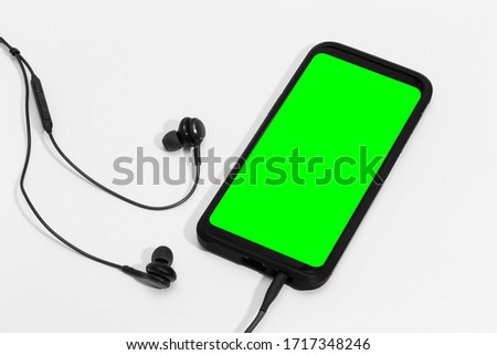 Smart phone with green screen and earphones on white background. Chroma Key green on screen