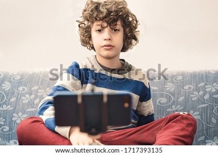 Young boy watching video on the internet with a smartphone relaxing on the sofa during coronavirus lockdown. People stay safe at home concept.