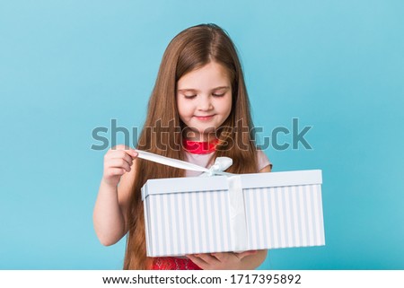 Happy child girl opening gift box on a blue background. Christmas time. Children's birthday.