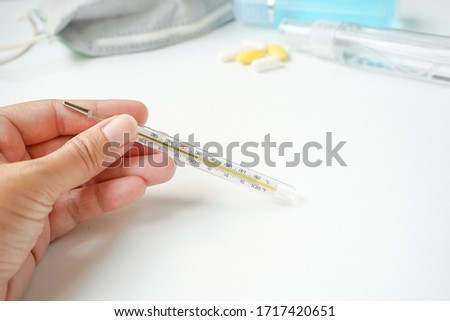 Hand holding mercury thermometer showing high temperature or have a fever with personal protective equipment to protect from Covid19 or Coronavirus disease, face mask, hand sanitizer and pill Royalty-Free Stock Photo #1717420651