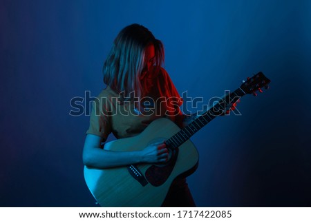 Short hair girl is enjoying her guitar in blue and red light.