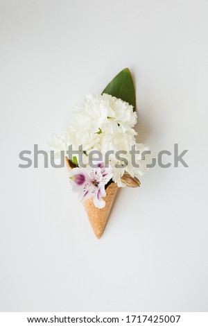 Flowers of white carnation and purple chrysanthemum in a waffle horn on a white background. Copy space, top view.