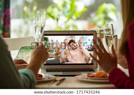 Man and woman sitting at the dining table, having dinner, drinking Champagne and having video call with senior parents on laptop. Staying home, quarantine and social distancing celebration of event.  Royalty-Free Stock Photo #1717435246