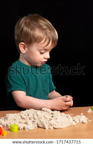 little boy plays kinetic sand on a table on a black background. isolate. multi-colored molds. close-up