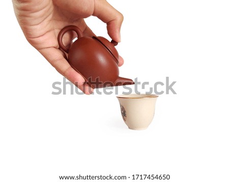 Hand pouring tea from Yixing Chinese teapot serving with a vintage white ceramic teacup in a tea ceremony isolated on white background with clipping path