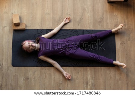 Modern girl is doing home yoga exercise. Lying on  floor in asana savasana. Zen relaxation after sports. Top view. Sleeps resting. Stretching Fitness Studio Online yogini trainer. silence meditation Royalty-Free Stock Photo #1717480846