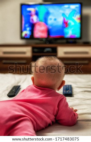 Lying girl infant with remote controllers and watching cartoons on TV screen