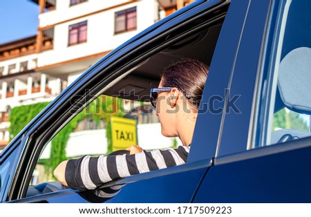 Beautiful female driver sitting in car.Beautiful female driver sitting in car on the background of a taxi sign.