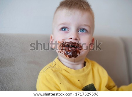 A boy with chocolate smeared all over his face and fingers happy and smiling
