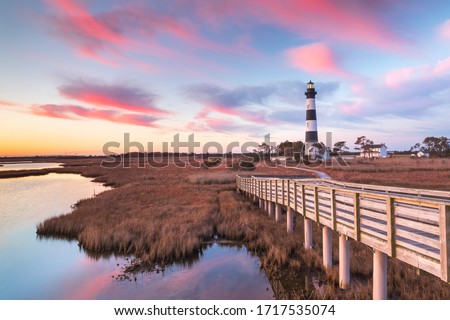 Clouds stream like pink ribbons in the sky over the marsh and lighthouse on Bodie Island on the Outer Banks of North Carolina. Royalty-Free Stock Photo #1717535074
