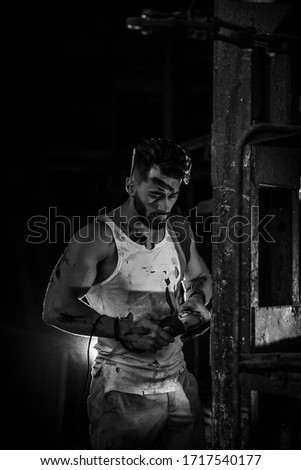 handsome man at the factory cuts metal, sparks fly, backlight shines on guy sports physique