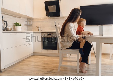Business mom is using online work laptop, woman spending time with her boy baby home.