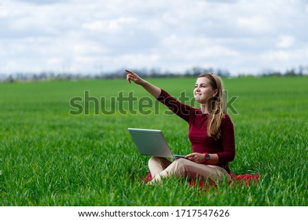 Young successful woman is sitting on green grass with a laptop in her hands. Work on the nature. Student girl working in a secluded place. New business ideas