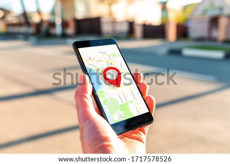 Male hand holding holding smartphone with online-a map on which the geolocation icon. In the background, a blurred street. Close up. Concept of online navigation and GPS Royalty-Free Stock Photo #1717578526