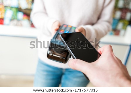 The seller holds a payment terminal, and the man pays for the purchase using a smartphone, online. Top view. Copy space. NFC concept, business and banking operations