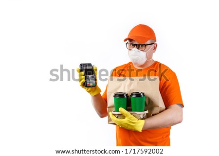 Cautious young man from a courier delivery service in a medical mask and gloves holds a cup of coffee in his hands, a package with an order and a terminal for cashless payment on a white background