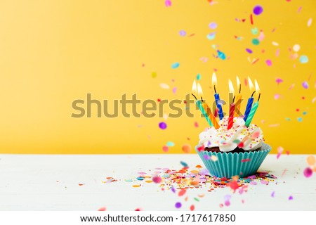 A colorful  birthday cupcake with seven candles and confetti on a yellow background