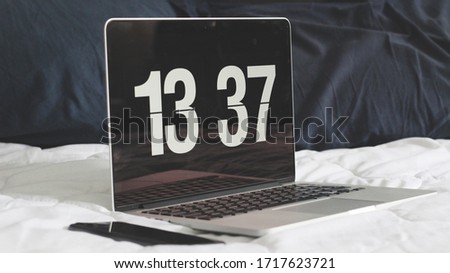 open laptop computer with vintage clock on a white bed and blue pillows