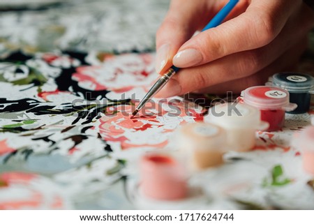 Young girl's hand draws with a brush painting by numbers on canvas. Creative hobby. Leisure activity at home during self-isolation COVID-19