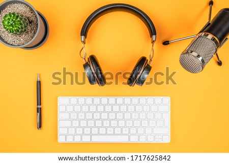podcasting and podcast recording concept, top view of microphone, headphones and computer keyboard on orange desk