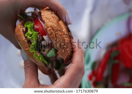 American cuisine. Fast food. Burger with beef, arugula, tomato, cucumber and sauce in hands. Summer picnic. Background image, copy space