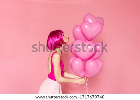 Image of young nice woman in wig holding balloons and making kiss lips isolated over pink background