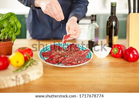 The chef is preparing beef carpaccio. He is topping the carpaccio with olive oil, sprinkling with freshly ground pepper and salt.