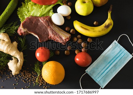 Quarantined healthy food. Raw beef steak, fresh vegetables, fruits and medical face mask on a black background.