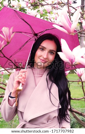 Beautiful, young girl with an umbrella among the branches of magnolia in the spring in the park. Happy woman on a background of pink magnolias in Kharkov.