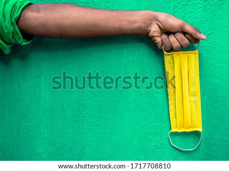 Man holding yellow face mask holding on his hand isolated on green background. Protective face mask on hand against Covid-19. Color face mask.Space for text