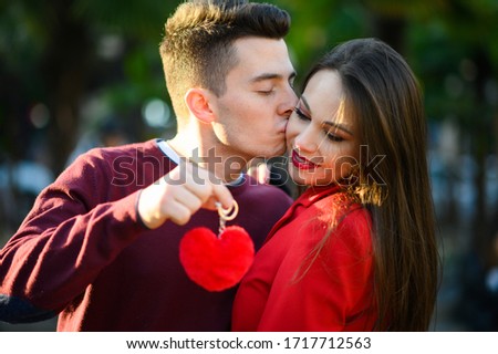 Young man kissing his girlfriend while holding a heart shaped pendant
