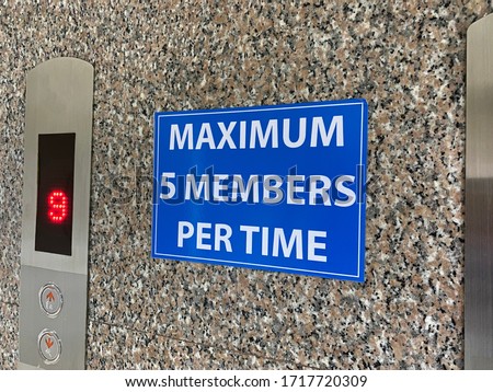 A sign warning message which has content is maximum five members per time is placed on a wall beside the elevator in an office during the pandemic of covid-19