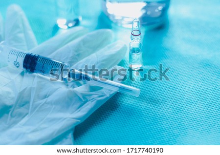 Syringe with medicine, ampoules and medical gloves on a blue background. Photo with blue tinted. Vaccination concept.