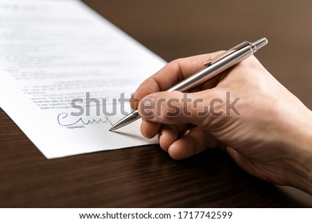 A businessman sits at an office Desk and signs a contract with a ballpoint pen