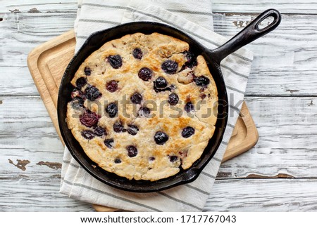 Fresh made homemade cherry cobbler baked in a cast iron pan over a rustic white wood table. Image shot from top view.