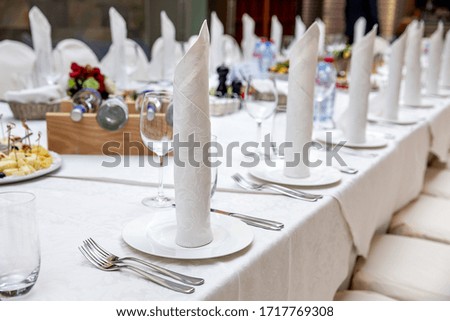Served banquet table prepared for a conference or a party and covered with a white tablecloth and with a folded cloth napkin on plate