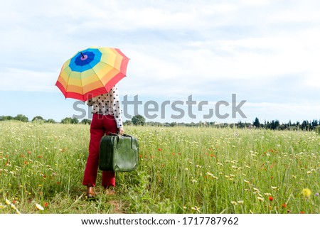 Romantic unrecognizable female standing in field holding multicolored umbrella enjoying dream freedom. Blooming beautiful flowers relaxing natural rural outdoor harmony background. Back view image