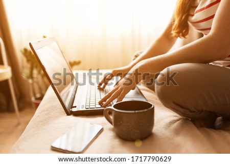 Shot of pretty young woman using her mobile phone while working with laptop sitting on the floor at home, stay at home, quarantine
