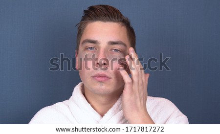 A young man puts patches on his face. Blue hydrogel patches for rejuvenating the skin of the face. Man sitting in a white coat. Close up