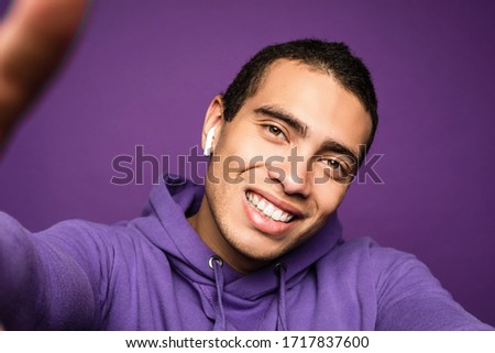 Young funny energetic man doing selfie and smiling. Look from phone. Isolated over purple background. Camera view