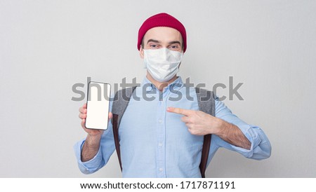 Joyful guy in a medical mask points at the phone, portrait, mock up, 16:9