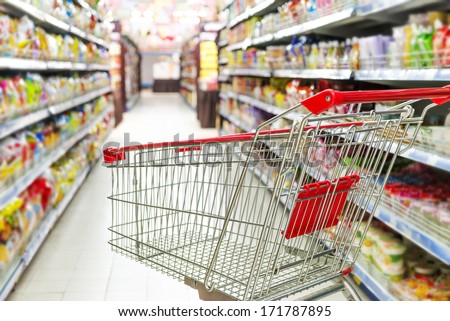 Supermarket interior, empty red shopping cart. Royalty-Free Stock Photo #171787895