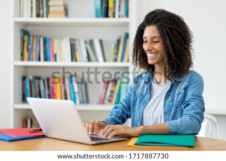 Laughing latin female student learning language online at computer at home