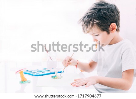 Boy sitting in white shirt painting with watercolor white clay figure.