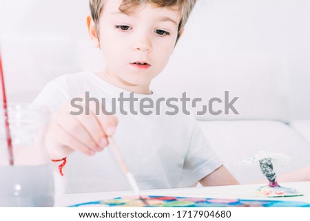 Attentive child painting with brush in hand and colored watercolors.