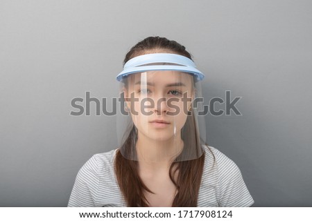 Young woman in a protective mask screen with a visor on a gray background Royalty-Free Stock Photo #1717908124