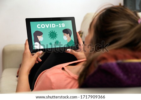 Coronavirus, COVID-19, quarantine time. Woman in home with tablet in her hands. In the screen an illustration of people with medical face mask.  Resting in a sofa.